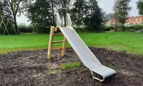 Een vrijstaande metalen glijbaan met een glad, zilverkleurig oppervlak en een houten trap met vier treden. De glijbaan heeft aan beide zijden veiligheidsleuningen bovenaan en een licht gebogen uiteinde voor een zachte landing.