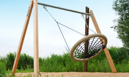 Nestschommel met ronde zitting van touw en netstructuur, bevestigd aan een metalen bovenbalk met houten A-frame staanders. Geschikt voor buitenspeelplaatsen zoals speeltuinen of schoolpleinen.