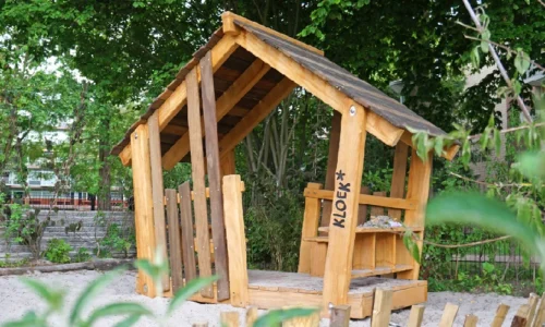 Speels vormgegeven houten speelhuisje “Bosmus” van robinia hout, gefotografeerd in een natuurlijke buitenomgeving. Het huisje staat op een groen terrein en straalt avontuur en buitenplezier uit.