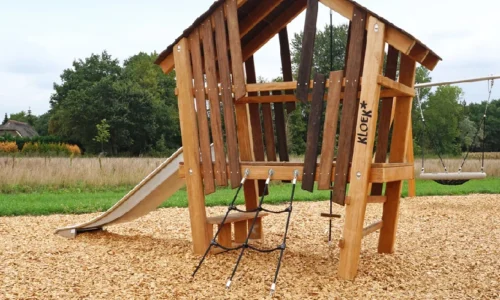 Speelhuisje Das” van robinia hout, levendig vastgelegd in een natuurlijke buitensetting. Het huisje met zijn speelse, organische vormen staat midden in het groen en straalt avontuur, rust en creatief buitenspel uit.